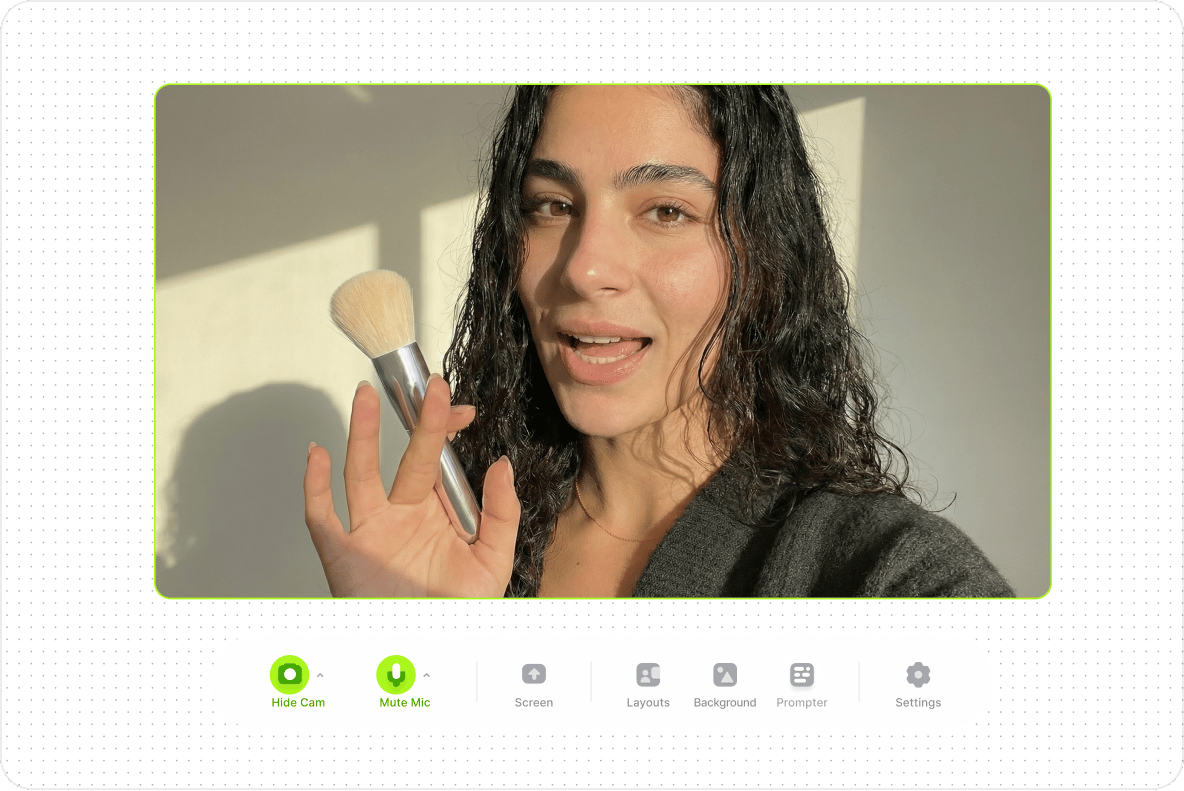Woman holding a makeup brush during a video recording with webcam recorder tool menu icons below.