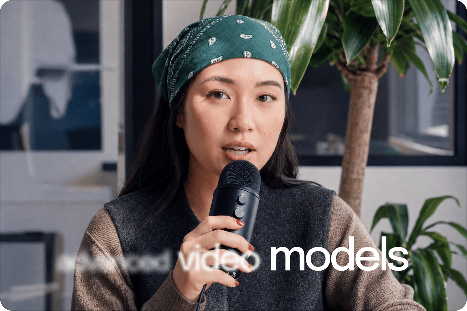 Woman in green bandana speaking into a microphone with caption text about video models