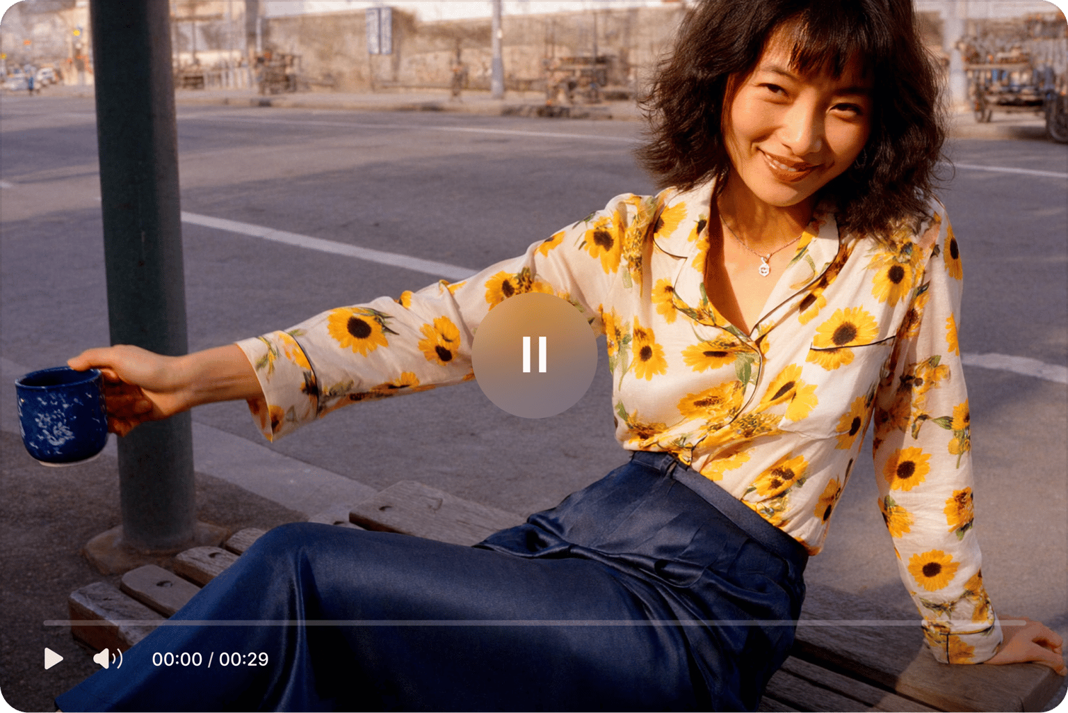Video player interface with a pause button over a high quality video of a smiling woman in a sunflower shirt holding a mug