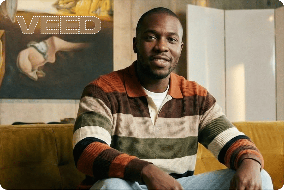 Man in striped polo sitting on a yellow sofa with a dashed outline selecting the VEED watermark to remove it.