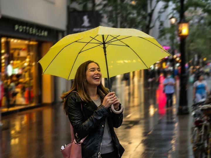 Unblurred photo of a woman laughing under a yellow umbrella in the rain