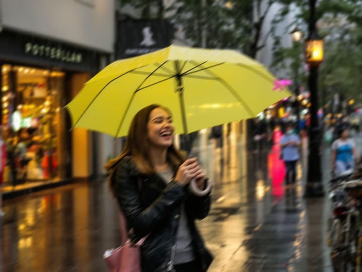 Blurry photo of a woman laughing under a yellow umbrella in the rain