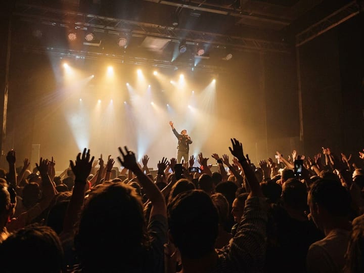 Unblurred photo of a concert crowd cheering at a lit stage