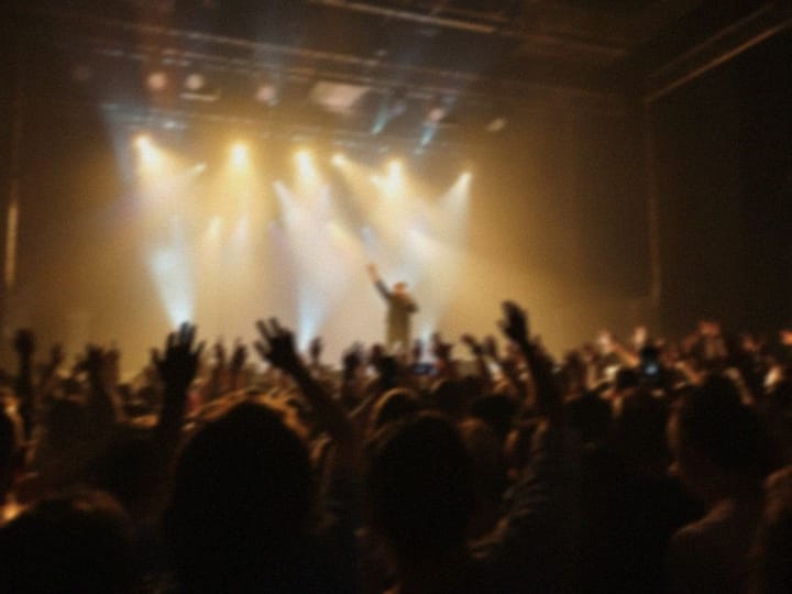 Blurry photo of a concert crowd cheering at a lit stage