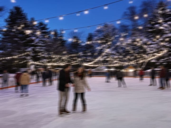 Blurry photo of people ice skating under string lights