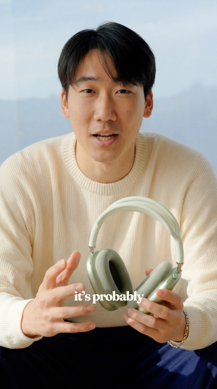 A presenter holding a pair of headphones up to the camera in a bright room